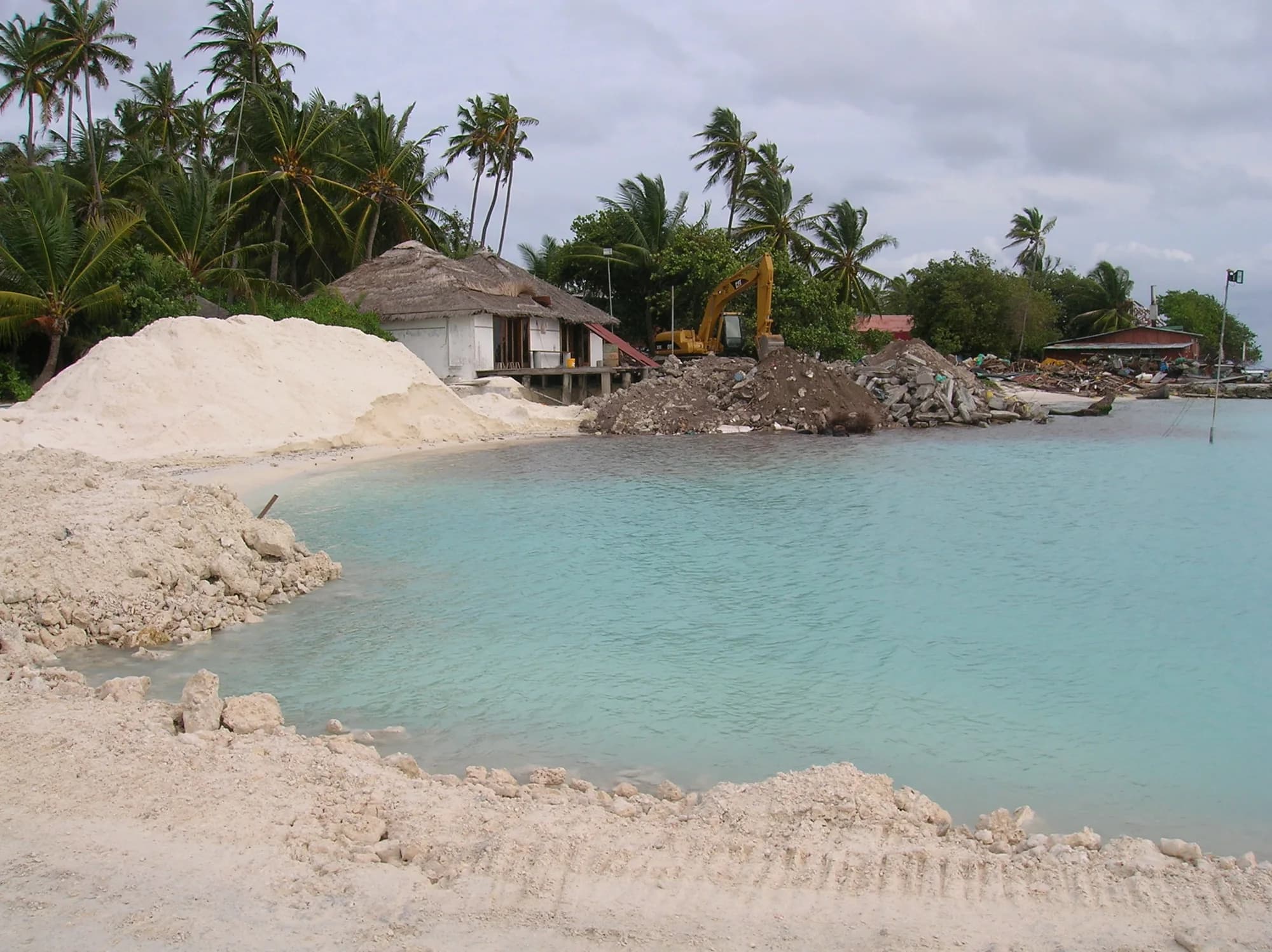 A large mound of dredged white sand stockpiled on the shore beside a resort building