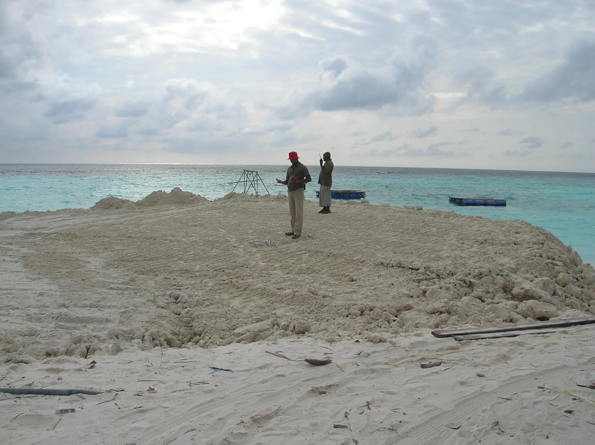 Two men checking levels on a freshly built sand bund, floating spoil pontoons moored beyond